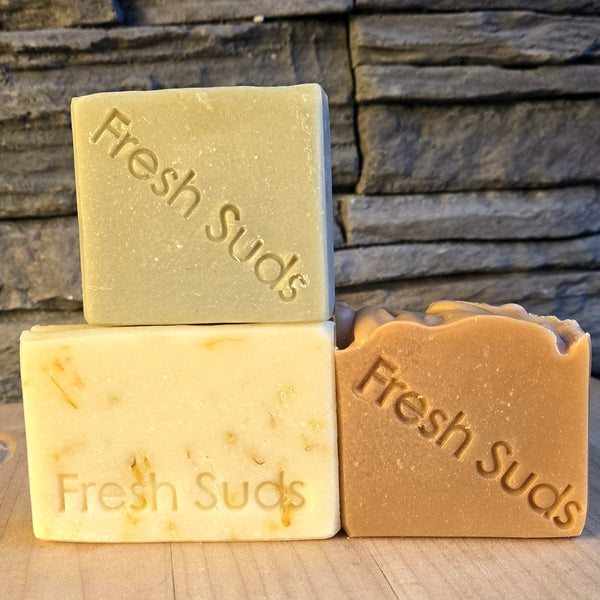 Sensitive Skin Soap Bundle: Forest Sunrise, Serenity Calendula and Rosemary Daydream bars on a wood board against a stone wall