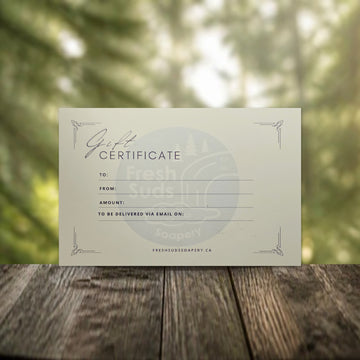 Fresh Suds Soapery gift certificate on a wooden table with a forest background