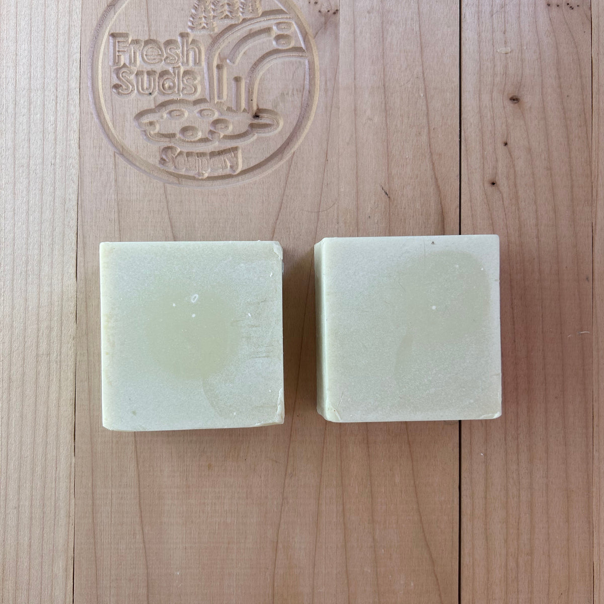 Two Olea Unscented soap bars on a wooden board with the Fresh Suds Soapery logo
