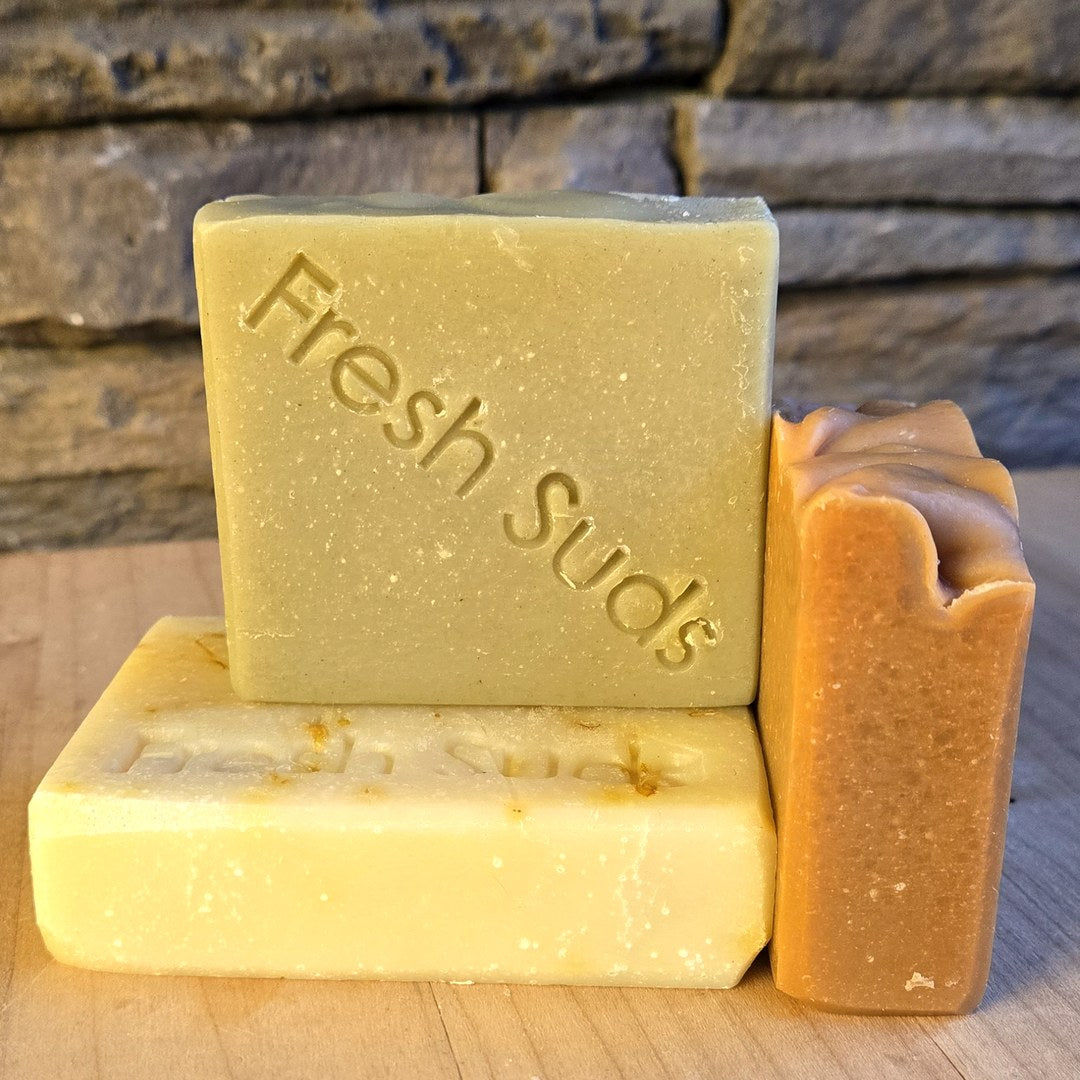 Sensitive Skin Soap Bundle: three Fresh Suds bars stacked on a wood board, stone wall behind