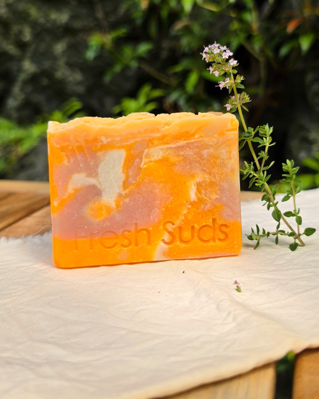 Golden Plumeria soap bar with cream and warm-orange marbling on natural linen beside a thyme sprig